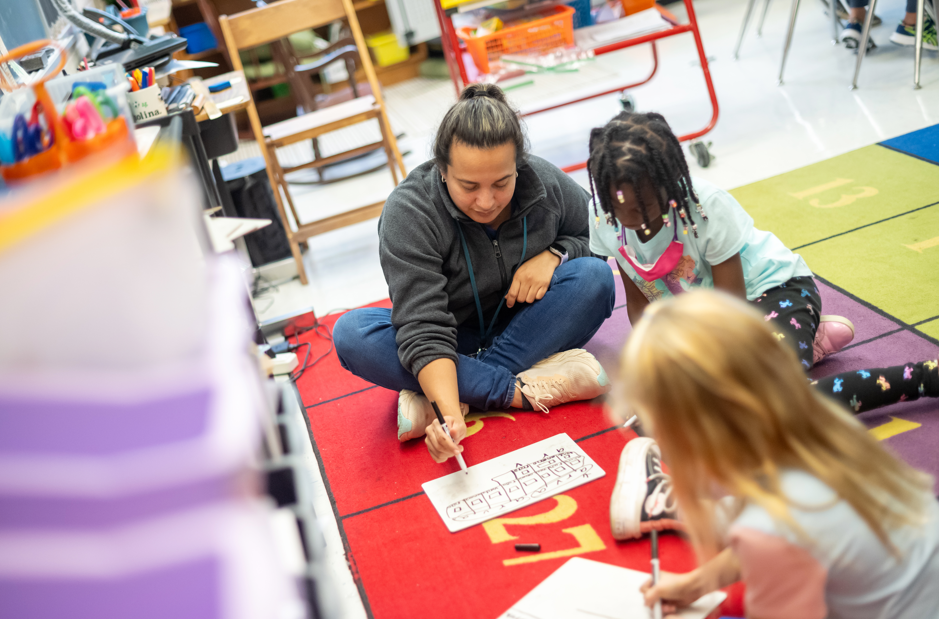 Pictured: Ms. Molina, a 2nd grade Immersion Teacher, working with a 2nd grader on a math center. 